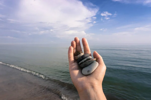 A hand holding a lot of stones on the coast of the Baltic Sea in summer during the tide