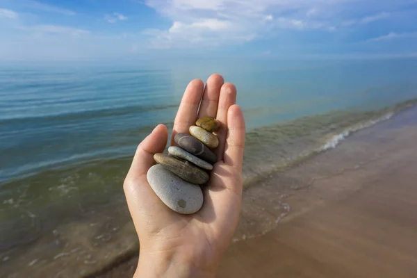 A hand holding a lot of stones on the coast of the Baltic Sea in summer during the tide