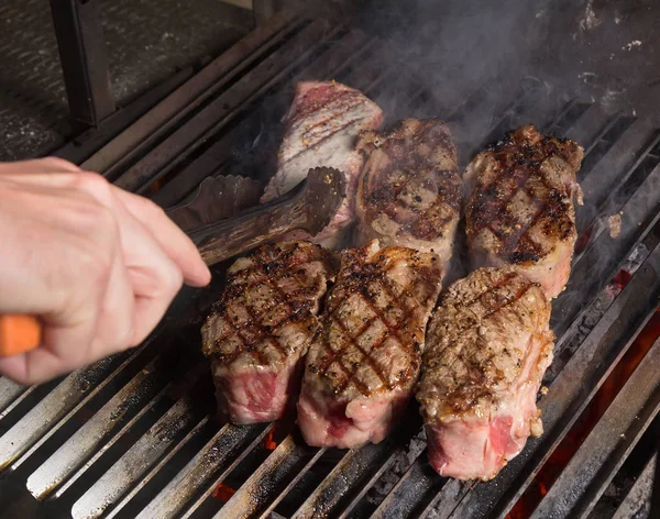 Turning steaks with spices on hot grill. — Stock Photo, Image