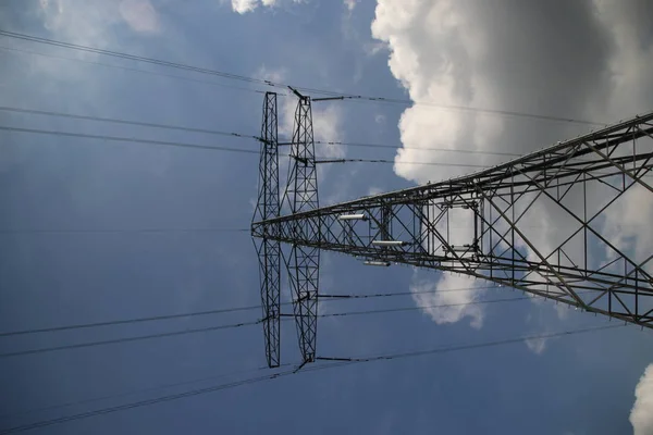 Metal tower for power lines in blue sky and sun with white clouds