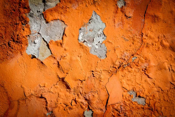 Orange plaster peeling off an old wall. Old dirty peeled plaster wall with falling off flakes of paint. Texture, pattern, background.