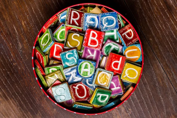 Lata cheia de azulejos cerâmicos coloridos com letras — Fotografia de Stock