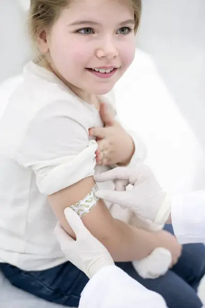 医師は 医療クリニックで注射後 小さな女の子の腕に石膏を貼り付けます — ストック写真