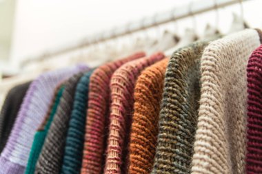 Nice warm colorful sweaters hang on hangers inside of a shopping mall. Beautiful clothes for winter autumn season. Fashion industry for women and men. Wool things for fall. Classic design. Merchandise in a shop. clipart