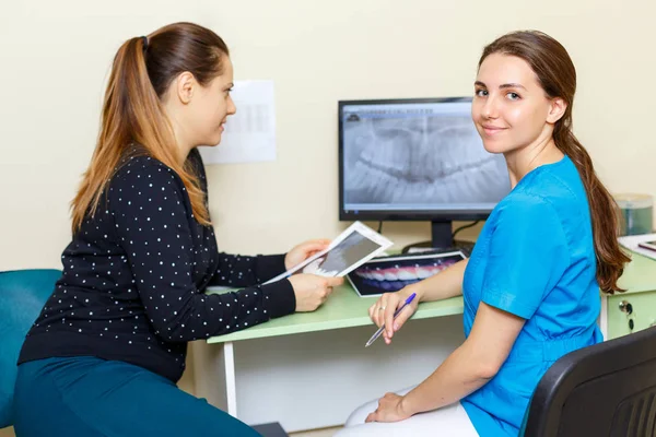 Dentyści Młoda piękna kobieta, patrząc na kamery i kobieta pacjenta dyskusji na zdjęciu RTG na komputerze leczenie dyskusji — Zdjęcie stockowe