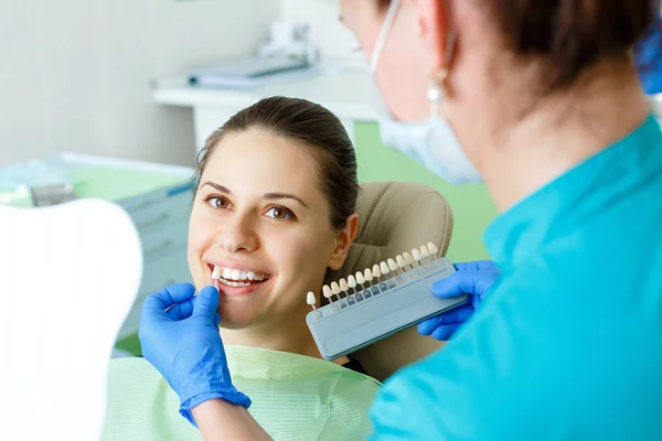 Dentist checking and selecting color of young womans teeth looking at the camera close up