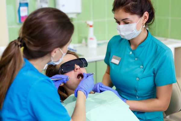 Hermosa mujer joven que recibe tratamiento dental en el consultorio de dentistas. dentista femenina con asistente de cerca —  Fotos de Stock