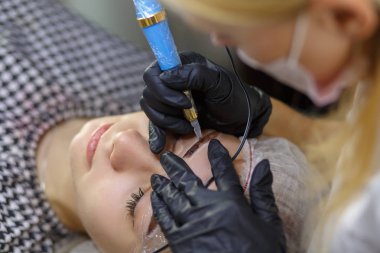 Microblading kaşlar iş akışında bir güzellik salonu. Renkli ona göz kaşları olan kadın. Kaşları için yarı kalıcı makyaj. Modelleri yüz ve kaş odaklanmak