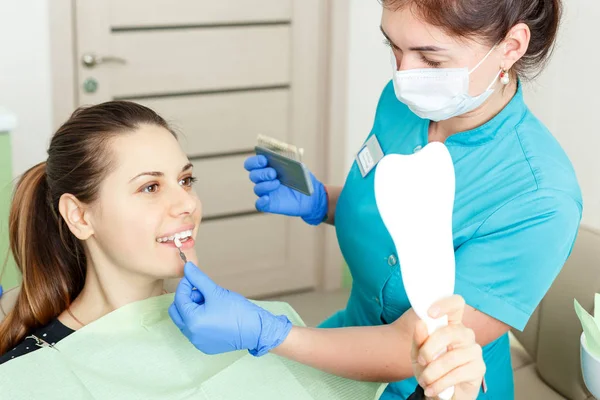 beautiful dentist checking and selecting color of young womans teeth