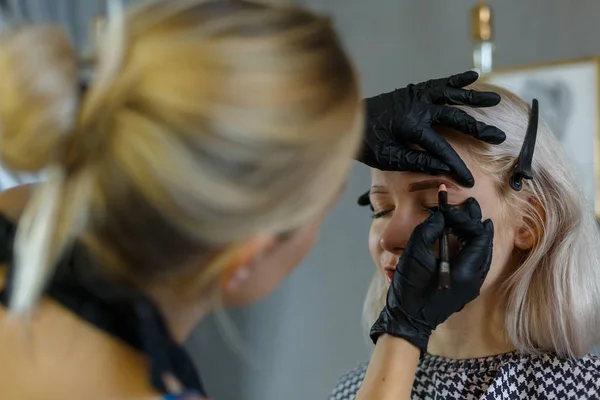 Maquiagem permanente para sobrancelhas. Closeup de bela mulher esteticista fazendo tatuagem de sobrancelha para rosto feminino. Procedimento de beleza . — Fotografia de Stock