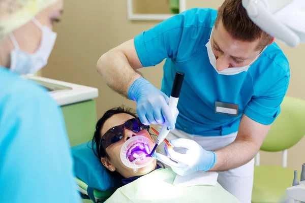 Dentista no trabalho na unidade odontológica com uma enfermeira e uma mulher doente deitada . — Fotografia de Stock