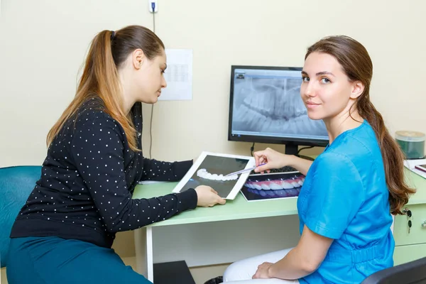 Giovane donna dentisti guardando la macchina fotografica e paziente donna discutendo la fotografia a raggi X sulla discussione trattamento del computer — Foto Stock