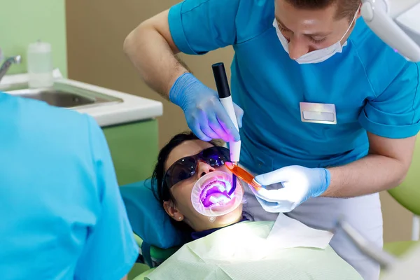 Dentista en el trabajo en la unidad dental con una enfermera y una mujer mintiendo paciente. Cirugía —  Fotos de Stock