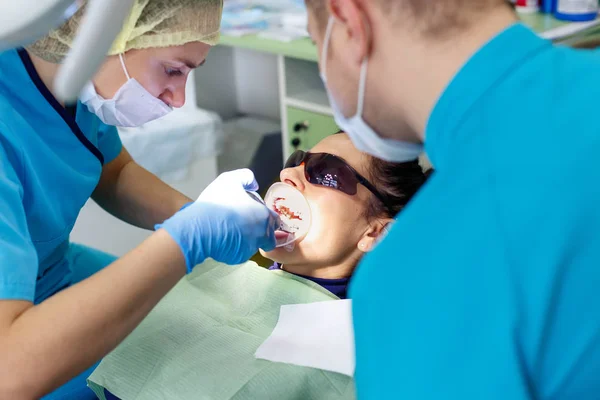 Dentista tratando dientes a paciente mujer en clínica. Médico estomatólogo profesional femenino en el trabajo. Equipo dental en segundo plano. Control dental. . —  Fotos de Stock