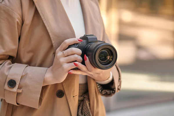 Close-up woman holding professional photo camera, beige