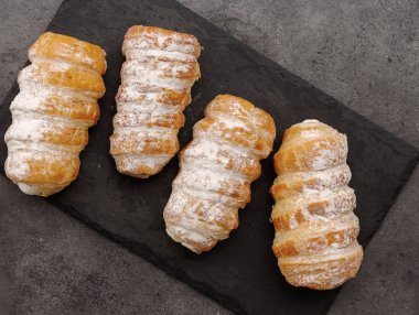 Siyah bir taş tahta üzerinde pudra şekeri ile ezilmiş dört kruvasan. Üstte görüntü