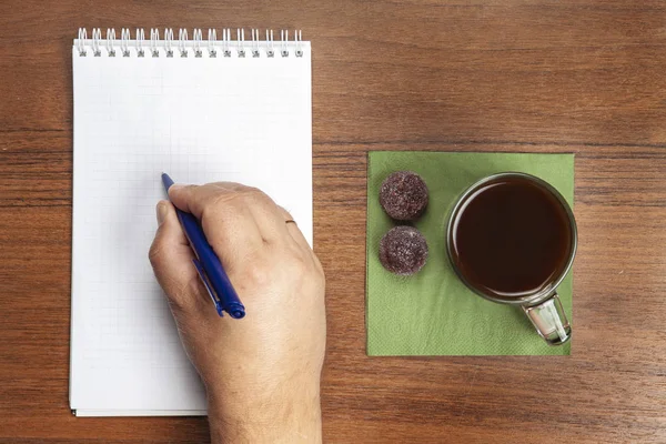 次にコーヒーのマグカップは 手はノートにペンで書いて — ストック写真