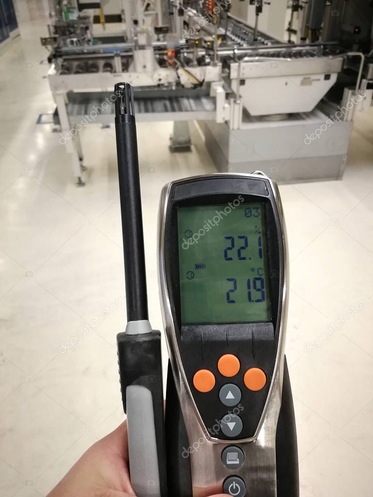 The hand of a person holds a device for measuring temperature and humidity. Measures in an industrial environment