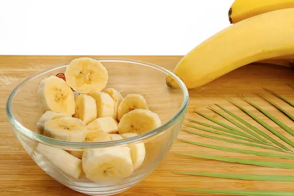 Sliced banana lies in the plate. Plate, fern bush, bananas lie on a wooden board. White background, isolate