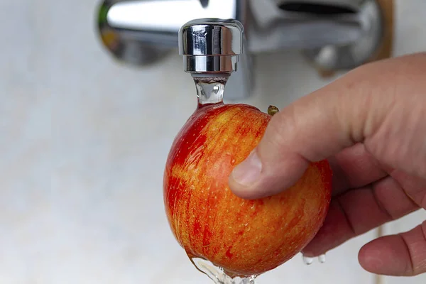 A hand is holding a red apple under the tap. Wash the apple.