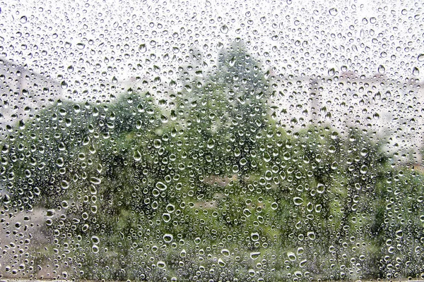 Raindrops on the window against the background of houses and trees — Stock Photo, Image