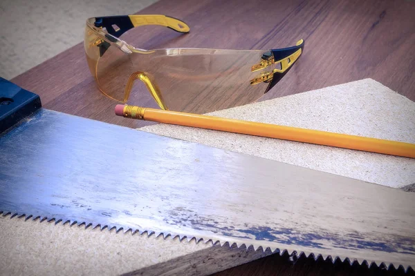 Scie sur bois, crayon pour le marquage et lunettes reposent sur une planche en bois — Photo