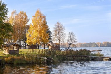 Sonbahar ağaçları ve ahşap saçaklar ile büyük bir gölün kıyısı.