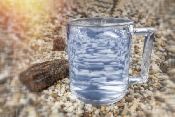 Un vaso de agua está sobre la arena . — Foto de Stock