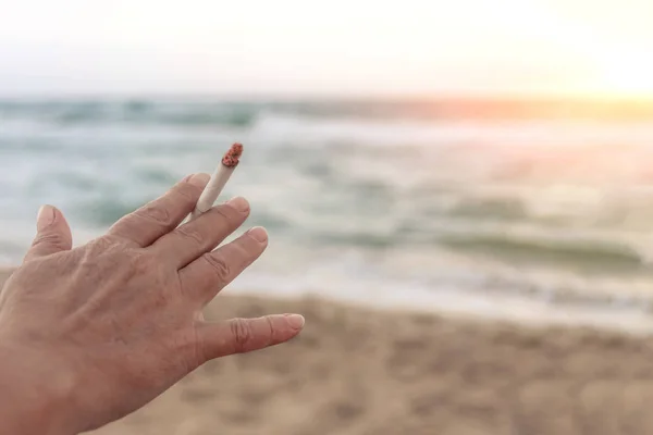 A keze cigarettát tart az esti tengeri. — Stock Fotó