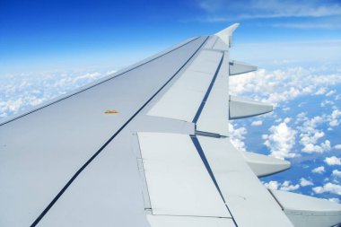 Bulutların üzerinde uçan bir uçağın kanadı. İnsanlar uçağın penceresinden gökyüzüne bakıyorlar, seyahat etmek için hava ulaşımını kullanıyorlar..