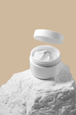 Kahverengi arka planda beyaz plastik plastik kozmetik kavanozu ve taş maketi var. Seçici Odaklanma.