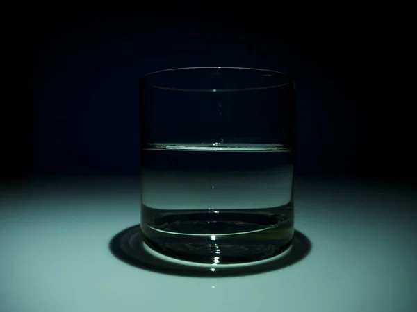 Medio vaso lleno con agua en la oscuridad. Fondo negro — Foto de Stock