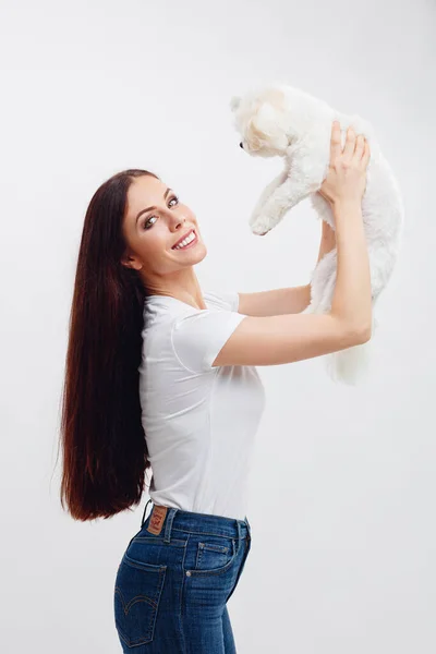 Menina morena bonita sorrindo com os dentes, segura cachorro maltês branco e seu cabelo voa — Fotografia de Stock
