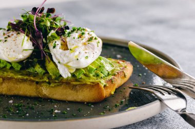 Guacamole ve haşlanmış yumurta bruschetta yanında yeşillik ve dilimlenmiş avokado.