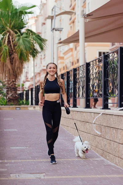 Mulher desportiva e cão correndo juntos dentro das ruas da cidade . Imagens Royalty-Free