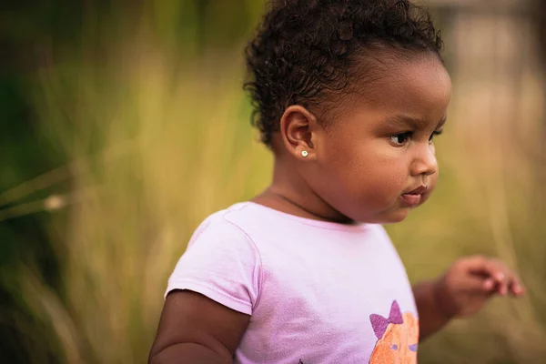 Retrato de doce menina afro-americana vestindo bonito roupa colorida e caminha na grama ao ar livre Fotografia De Stock