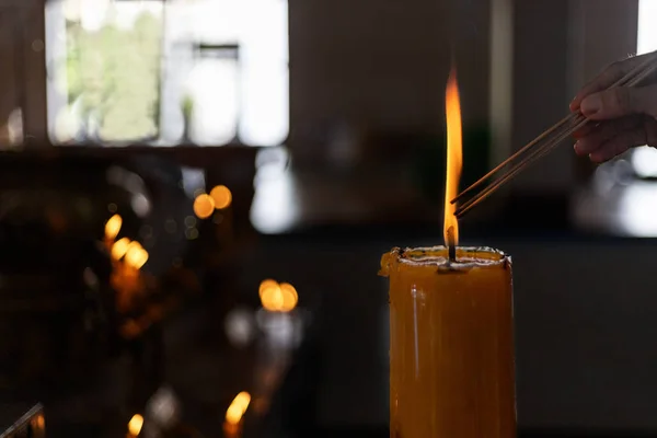 Buddhist Lent concept. Women hand lighning the incense from big candles in the Buddhist temple Close up light form candles. Process with low key style. With copy space for text or design.