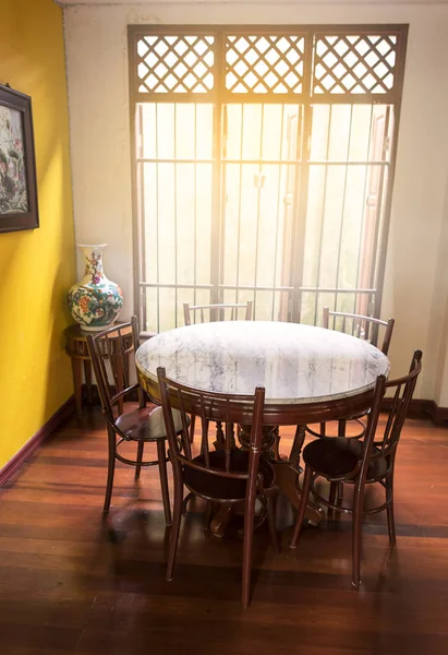 Pencere yakınında ahşap yuvarlak masa ve sandalye chiness tarzı ahşap zemin ve sarı duvar da Nilüfer chiness resim ışık ışığı var