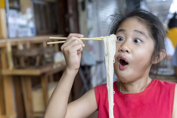 Asijská holčička s červenými šaty, které jedí malé nudle polévku s hůlky — Stock fotografie
