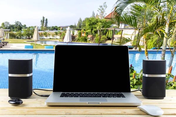 Work desk laptop mouse and speakers on wood table with garden and swimming pool background. With copy space for text or design