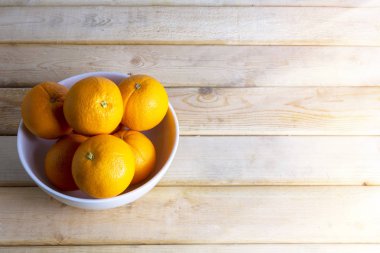 Tahta masadaki beyaz kasede taze portakallar. Metin veya tasarım için kopyalama alanı ile.