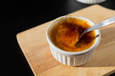 Şekerli beyaz ramekin içinde ev yapımı creme brulee siyah arka planda siyah kaşıkla çatırdıyor ve fotokopi çekiyor. Fransız tatlı creme brulee