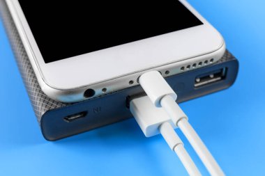 Fotokopi alanı ile mavi arkaplanda elektrik bankasıyla şarj olan akıllı telefonu kapat. Beyaz USB kablosuyla elektrik bankasıyla akıllı telefon şarj ediliyor.