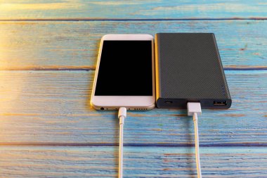 Fotokopi alanı olan mavi arka plandaki güç bankasıyla akıllı telefonu kapatın. Beyaz USB kablosuyla elektrik bankasıyla akıllı telefon şarj ediliyor.