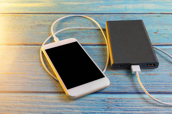 Close up smartphone charging with power bank on blue background with copy space. Smartphone charging with power bank by white USB cable.