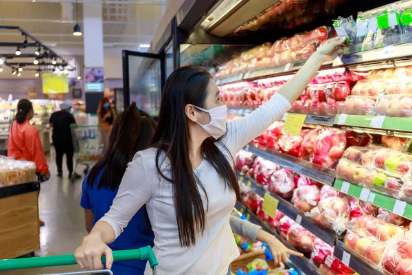 Asian woman wear face mask push shopping cart in suppermarket departmentstore. Girl, looking grocery to buy  fruit. Women wearing protective face mask hold shopping cart New normal after covid-19.