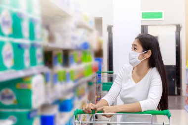 Asyalı kadın yüz maskesi takıyor süpermarkette alışveriş arabası itiyor. Coronavirus krizi ya da kovid19 salgını sırasında bir şeyler almak isteyen bir kız. Koruyucu yüz maskesi takan kadınlar yeni normal kavram