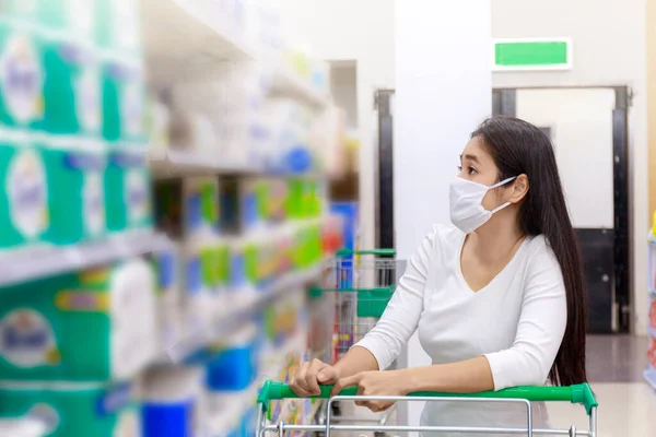 Asian woman wear face mask push shopping cart in supermarket. Girl looking grocery to buy something During coronavirus crisis or covid19 outbreak. Women wearing protective face mask new normal concept