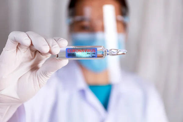 Covid-19 koronavirüs aşısı. Bilim adamının eli kapalı Covid-19 aşısını cam şişede göster. Doktorun elleri cam şişede Covid-19 aşısı tutan lateks eldiven takıyor. Sağlık ve Tıp Konsepti.