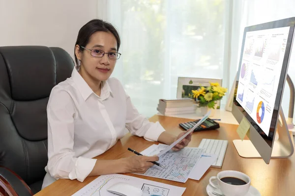 Business women smileing  wear glasses hands holding paper and pencil. business people analysis chart data on computer PC screen at office. Business at home concept.